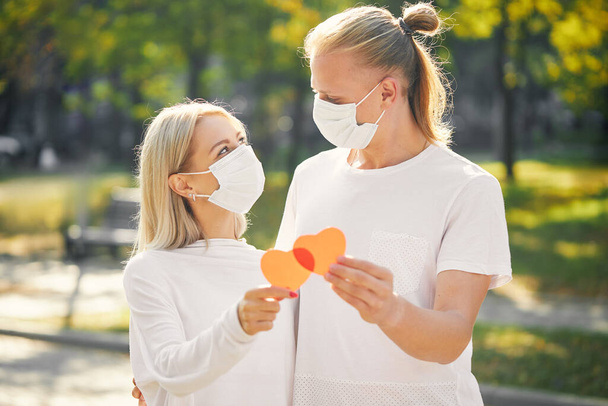 コロナウイルスやインフルエンザの流行の間に保護マスクを身に着けている赤い心臓を持つカップル。ウイルス及び疾病の予防.  - 写真・画像