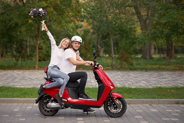 Joyeux jeune couple d'amour sur scooter rouge rétro à l'extérieur. Romantique sortir ensemble dans le parc - Photo, image