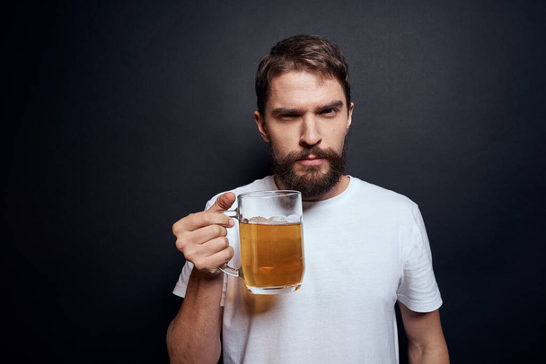 白いTシャツを着たビールのマグカップを手にした男は暗い隔離された背景で酒を飲み - 写真・画像