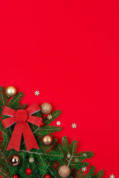 Weihnachtskarte von oben aus Tanne, Schleifen, goldenen Dekorationen, Konfetti, Schneeflocken auf rotem Hintergrund - Foto, Bild