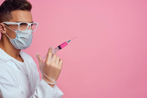 A doctor in a medical mask and gloves holds a syringe in the hands of an injection laboratory - 写真・画像