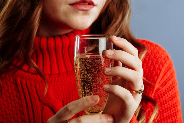 Close up view of hands holding cocktail on party. Woman in a red sweater holds a glass with champagne. - Zdjęcie, obraz