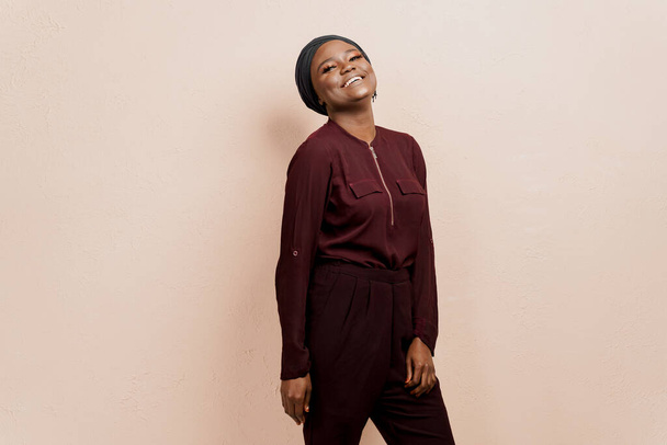 Muzułmańska czarna dziewczyna się uśmiecha. Afrykanka ubrana w strój narodowy i szalik odizolowana na brzoskwiniowym tle - Zdjęcie, obraz