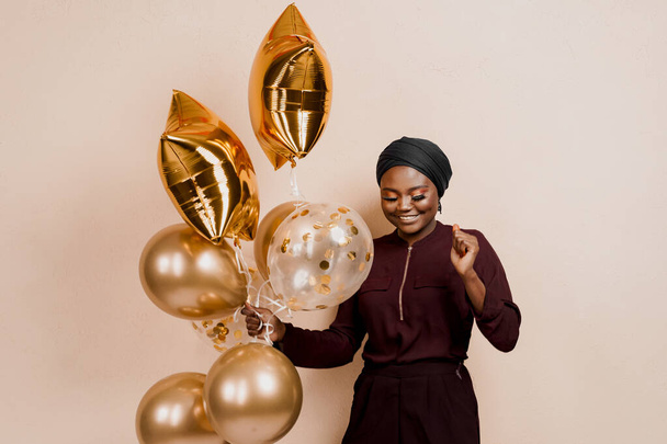 Muslim new year party with golden balloons for black woman. African attractive girl celebration of the end of year. Happy emotion - Foto, Imagem