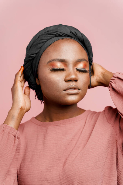 Muslim woman with closed eyes close-up. Relax and meditation. African black attractive girl vertical portrait isolated on pink background - Foto, Imagem