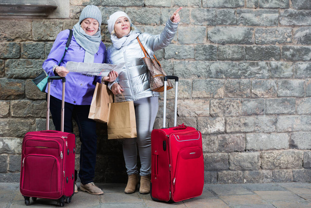 Ηλικιωμένες κυρίες με βαλίτσες και χάρτη κοντά σε πέτρινο τοίχο - Φωτογραφία, εικόνα