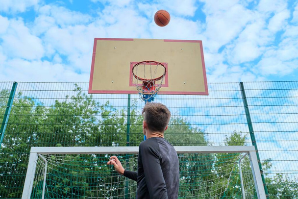 Teenager boy jumping with ball playing street basketball, back view - Φωτογραφία, εικόνα
