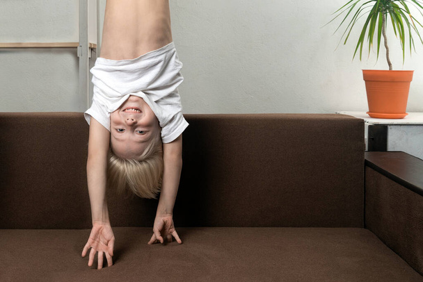 Boy is upside down over sofa. Funny child hangs upside down - Photo, Image