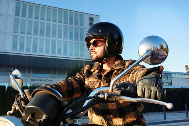 Young bearded biker man on motor bike outdoors exploring city streets. - Фото, изображение