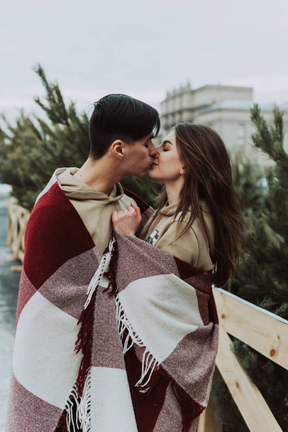 Una giovane coppia che si bacia in inverno sullo sfondo del mercatino dell'albero di Natale in città. amore, vacanze invernali e concetto di persone - Foto, immagini