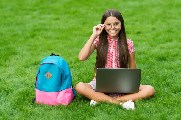 teen girl use computer on green grass in park. child with backpack and notebook. new technology in modern life. study. happy kid in glasses working on laptop. online education. back to school - Photo, Image