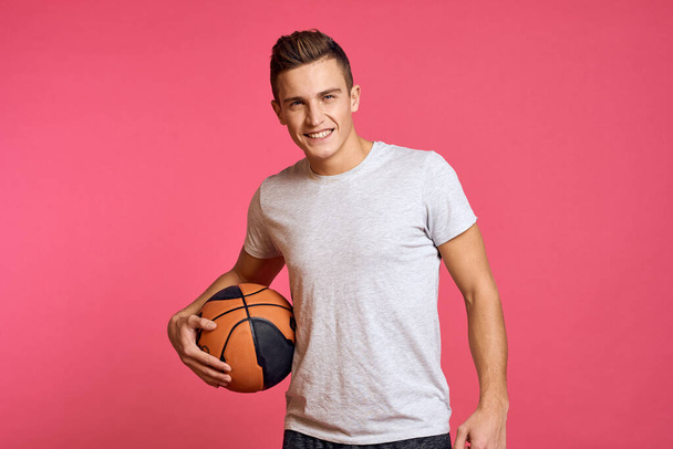 Guy avec une balle de basket sur un fond rose dans un t-shirt blanc vue recadrée Sport modèle séance d'entraînement - Photo, image