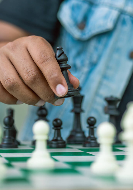 Chess game on a green board, one hand holds a black bishop - Foto, afbeelding