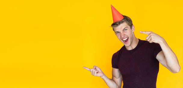 uomo allegro su uno sfondo giallo con un cappello festivo sulla testa. Concetto di festa di compleanno - Foto, immagini
