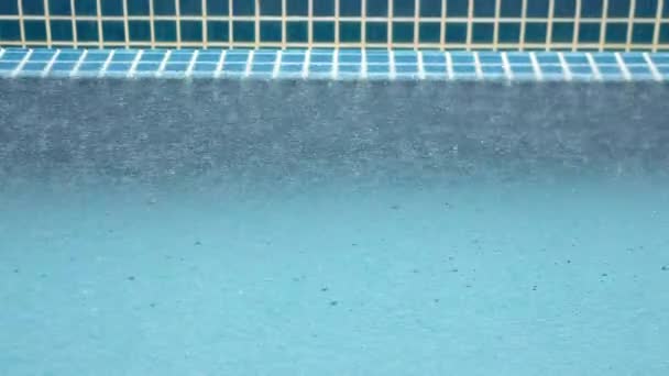 Lluvia tropical de verano salpicando en la piscina. Primer plano de la piscina durante la tormenta y las gotas de lluvia cayendo al agua  - Metraje, vídeo