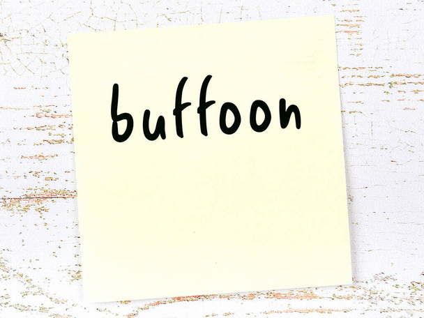 Yellow sticky note on wooden wall with handwritten word buffoon - Fotó, kép