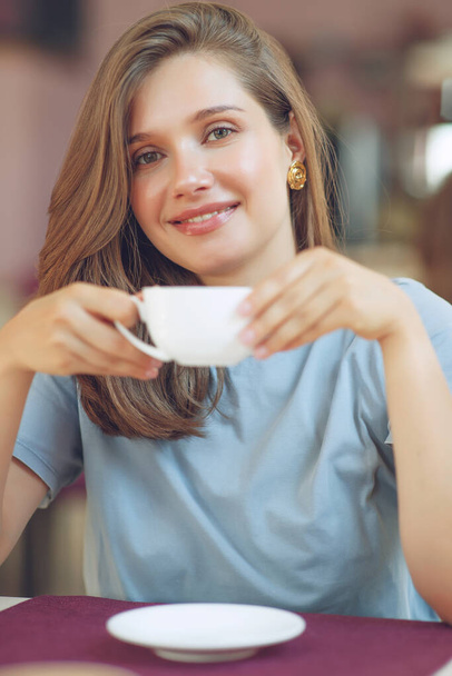 Mujer madura pensativa se sienta en una cafetería sosteniendo una taza de café. Una mujer de mediana edad bebe té mientras piensa. Relajarse y pensar mientras bebe café. - Foto, Imagen