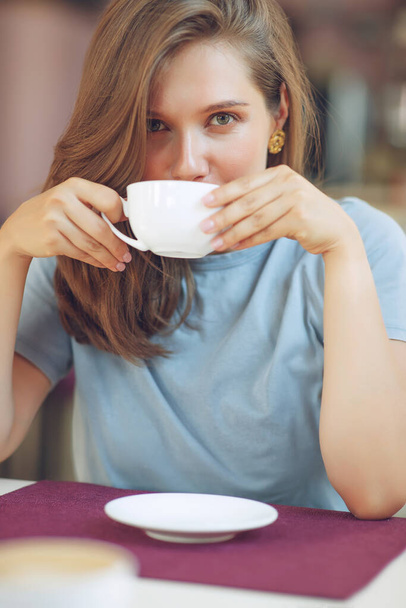 Μια ώριμη γυναίκα κάθεται σε μια καφετέρια κρατώντας μια κούπα καφέ. Μια μεσήλικη γυναίκα πίνει τσάι ενώ σκέφτεται. Χαλαρώνοντας και σκεπτόμενος πίνοντας καφέ. - Φωτογραφία, εικόνα