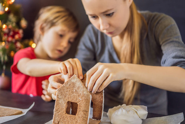Young mother and kid making gingerbread house on Christmas eve - Valokuva, kuva