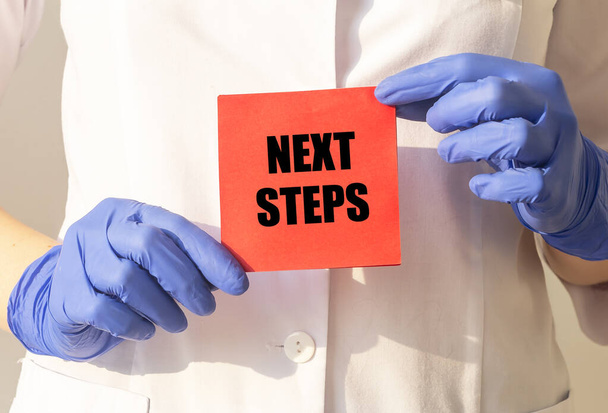 Text next steps on red paper note in doctor hands in protective gloves, future in medicine concept - Foto, afbeelding