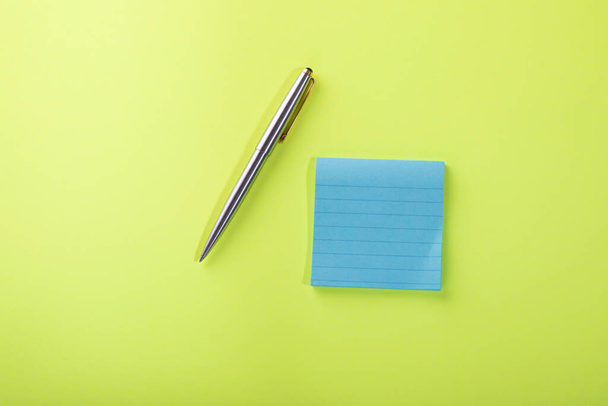 Cuadrado azul pegajoso bloc de notas con bolígrafo de plata sobre fondo verde. - Foto, Imagen