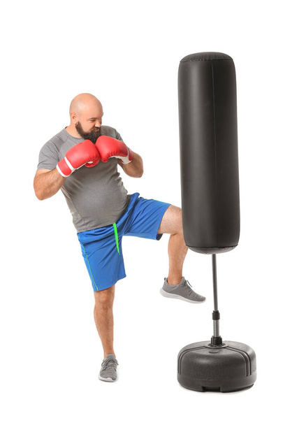 Overweight man in boxing gloves hitting punching bag on white background. Weight loss concept - Foto, afbeelding