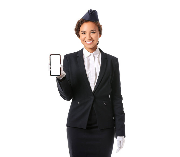 Beautiful African-American stewardess with mobile phone on white background - Photo, Image
