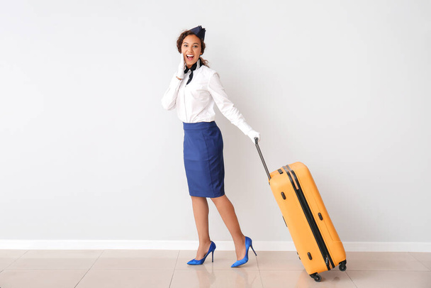 Mooie Afro-Amerikaanse stewardess met bagage bij grijze muur - Foto, afbeelding