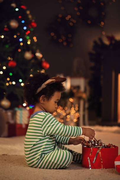 Милая афро-американская девочка с подарком дома в канун Рождества - Фото, изображение