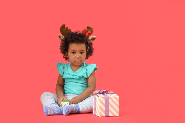 Cute African-American baby girl with Christmas gifts on color background - Fotoğraf, Görsel