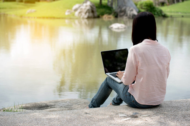 Mujer asiática sentada parque verde usando ordenador portátil. Mujer que trabaja en el negocio empresario feliz portátil utilizando portátil con las manos escribiendo en la oficina del teclado en casa durante el período de cuarentena coronavirus - Foto, Imagen
