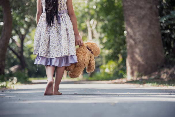 Sad girl hugging teddy bear sadness alone in green garden park. Lonely girl feeling sad unhappy walking outdoors with best friend toy. Autism child play teddy bear best friend. Family violence concept - Photo, Image
