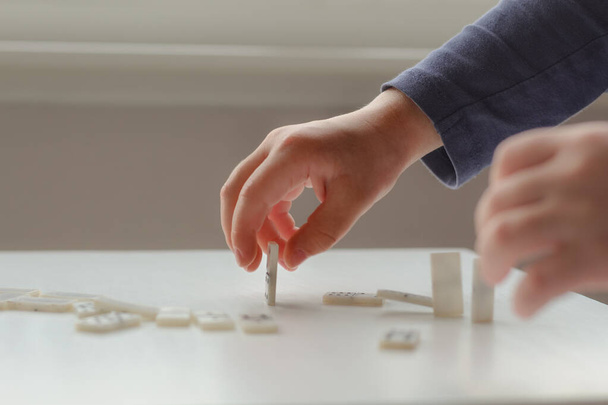 Dziecko gra w domino. Dłonie układają kostki domina. Koncepcja gier planszowych o samoizolacji. - Zdjęcie, obraz