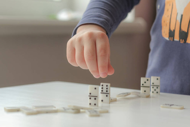 Un bambino gioca a domino. Le mani sistemano le nocche del domino. Il concetto di giochi da tavolo sull'autoisolamento. - Foto, immagini