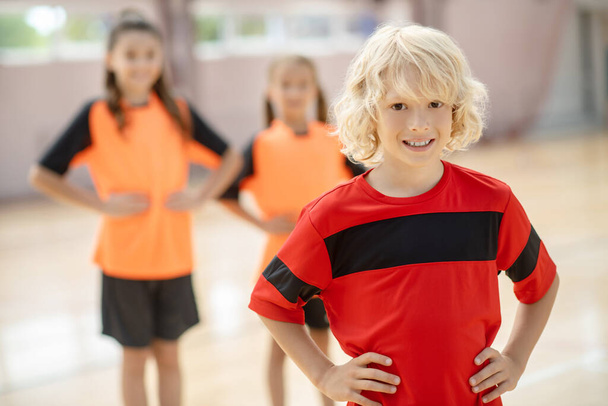 Blonde boy in red tshirt standing with hands on hips - 写真・画像