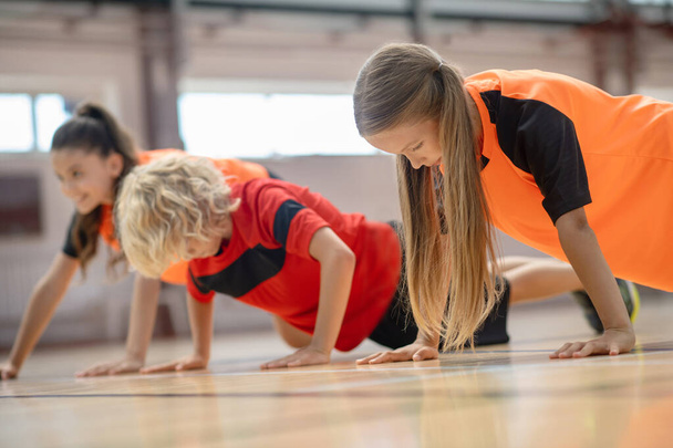 Kids in bright sportswear doing push ups and looking concentrated - Φωτογραφία, εικόνα