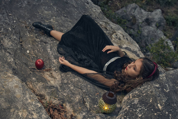 girl lying over a rock with a latern and a poisoned red apple , Snow White looks for halloween - Photo, Image