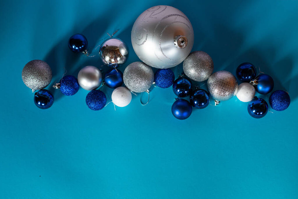 Shiny Christmas balls in blue, white and silver are arranged in a row on a turquoise background with a space for text. - Foto, Bild