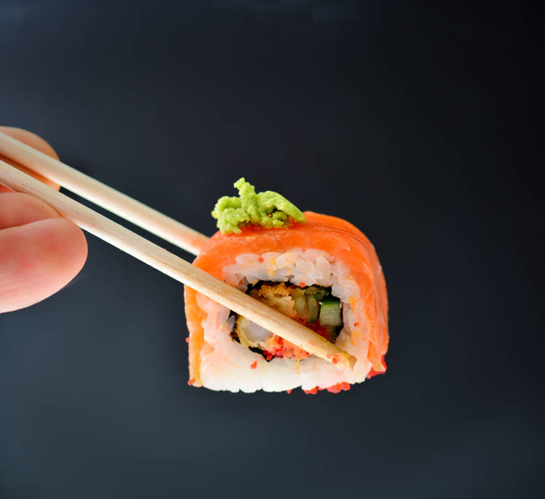 man holding wooden chopsticks sushin, on top of wasabi sushi. dark background. concept of japanese restaurants, meeting friends date, birthdays. - Fotografie, Obrázek