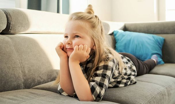 Little girl child watching TV at home lying on the couch. A kid watches cartoons and educational programs - Photo, Image