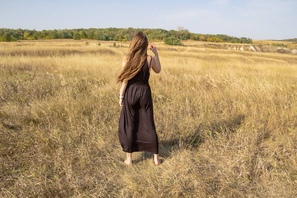 Pretty young dark haired woman in black dress stand in field. Beautiful girl outdoor in the field enjoy with freedom - Fotoğraf, Görsel