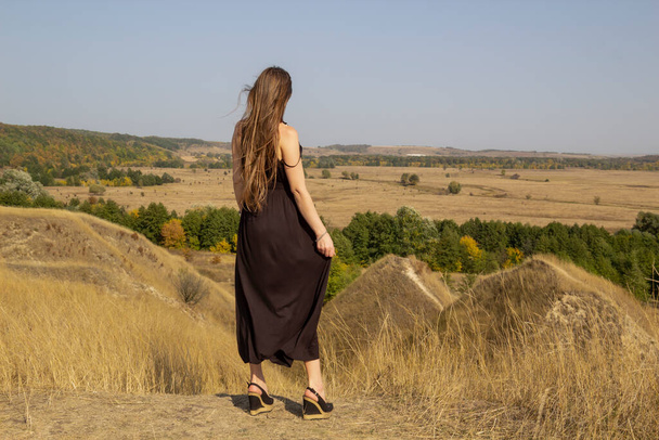 Krásná mladá tmavovlasá žena v černých šatech stojí v poli. Hezká dívka venku v terénu vychutnat se svobodou - Fotografie, Obrázek