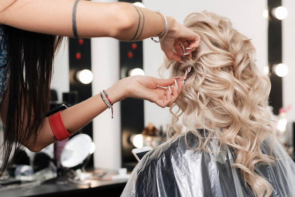 A female hairdresser makes festive blonde curls in a beauty salon. - Photo, Image