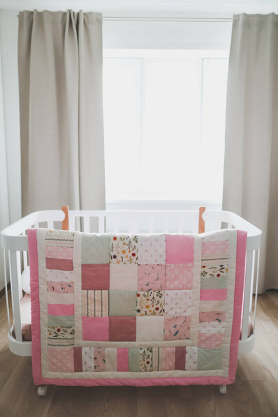 Cozy baby cot with pink patchwork blanket. Bedding and textile for children nursery. Photo of pink and white baby girl crib - Photo, Image