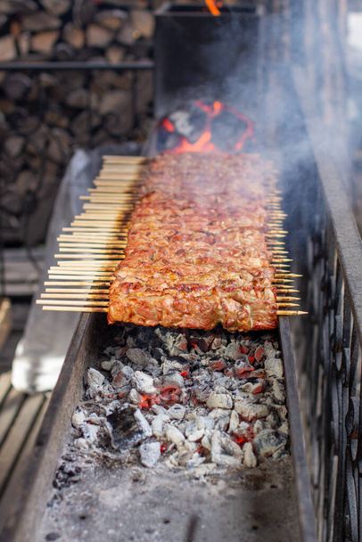 Spousta kebabů v řadě na grilu. Kebaby natažené na dřevěných špejlích v pouliční kavárně. Proces vaření kebabů se spoustou kouře. - Fotografie, Obrázek