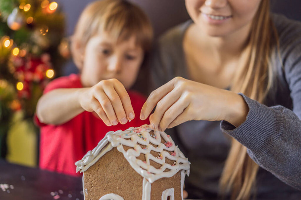 Young mother and kid making gingerbread house on Christmas eve - Фото, изображение