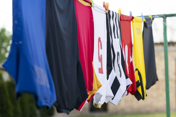 Bunte Kleider hängen zum Trocknen an einer Wäscheleine. Fußballtrikots  - Foto, Bild
