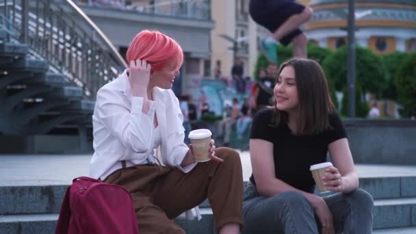 Twee jonge vrouwen die praten en lachen op de granieten trap en koffie drinken - Video