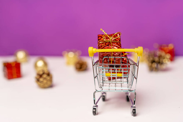 Koncept novoroční dovolené prodeje. Mini vozík s dárky na fialovém pozadí s roztroušené vánoční dekorace kolem - Fotografie, Obrázek