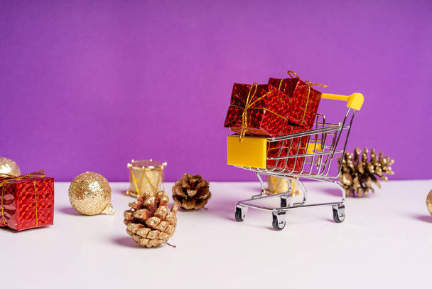 Η έννοια των πωλήσεων της Πρωτοχρονιάς. Μίνι καλάθι με δώρα σε μωβ φόντο με διάσπαρτα χριστουγεννιάτικα στολίδια γύρω - Φωτογραφία, εικόνα